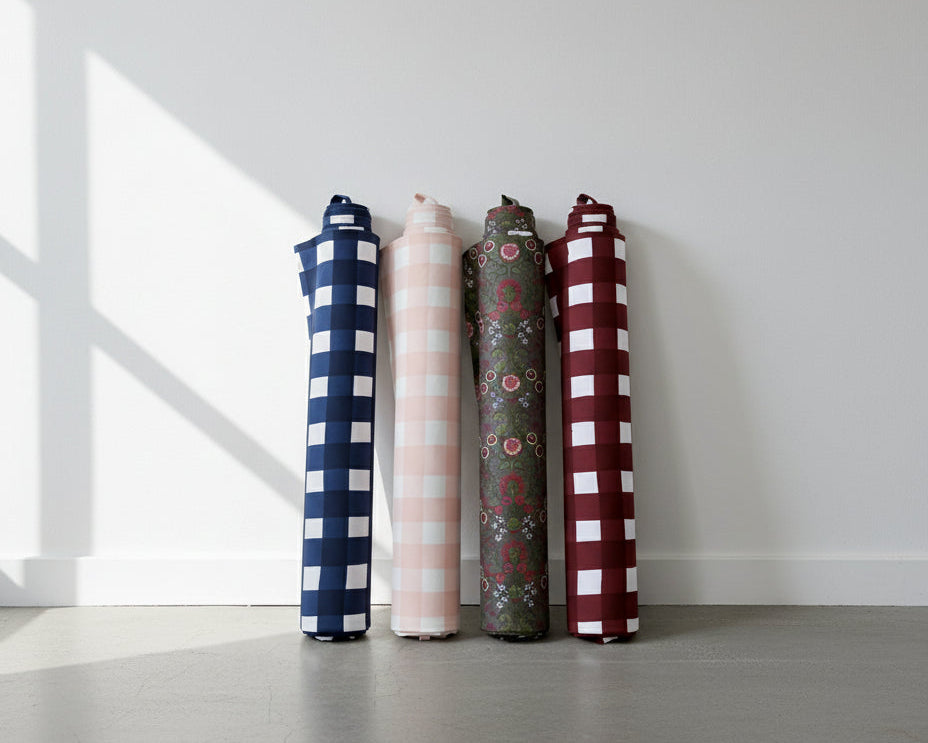 Four rolled-up fabrics in different patterns and colors against a white wall.